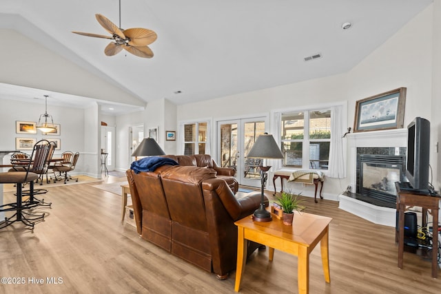 living room featuring light wood finished floors, baseboards, visible vents, a premium fireplace, and high vaulted ceiling