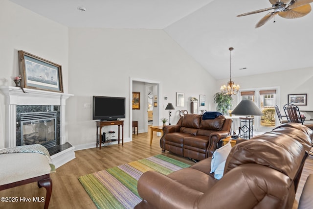 living area featuring light wood finished floors, baseboards, a premium fireplace, high vaulted ceiling, and ceiling fan with notable chandelier