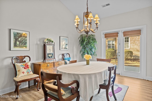 dining area with an inviting chandelier, light wood-style flooring, visible vents, and vaulted ceiling