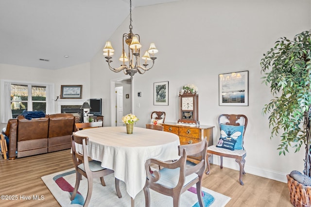 dining area with baseboards, an inviting chandelier, light wood-type flooring, a fireplace, and high vaulted ceiling