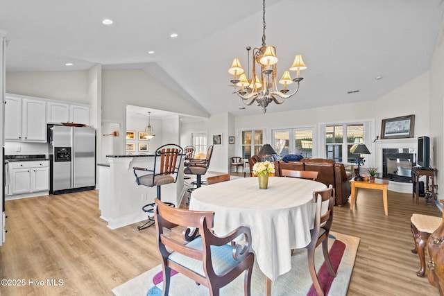 dining area with a notable chandelier, a fireplace, recessed lighting, high vaulted ceiling, and light wood-type flooring