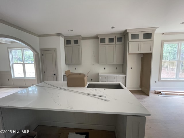 kitchen with a kitchen island, recessed lighting, arched walkways, glass insert cabinets, and baseboards