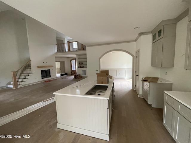 kitchen featuring arched walkways, a fireplace, dark wood finished floors, glass insert cabinets, and light countertops