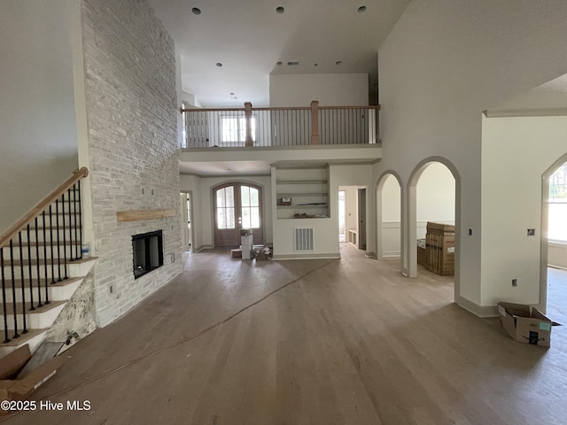 241 Juniper Creek Blvd, Pinehurst, NC 28374 - unfurnished living room featuring arched walkways, a stone fireplace, a towering ceiling, wood finished floors, and stairs