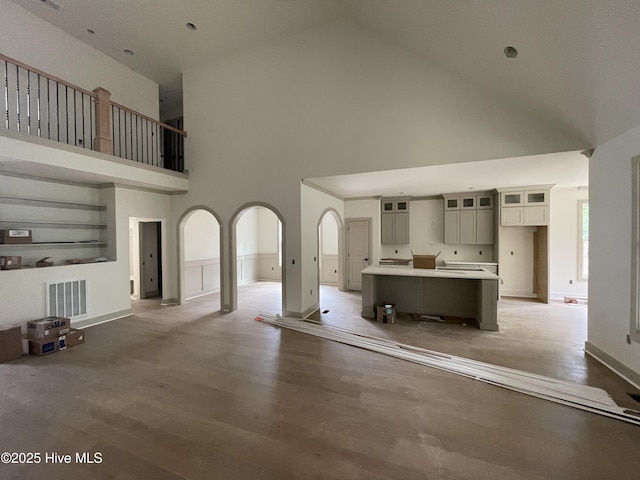 unfurnished living room with high vaulted ceiling, light wood finished floors, arched walkways, and baseboards