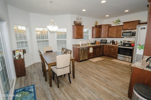 kitchen featuring pendant lighting, stainless steel appliances, light stone countertops, and light hardwood / wood-style flooring