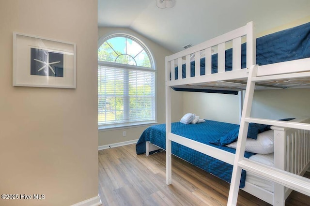 bedroom featuring lofted ceiling, visible vents, baseboards, and wood finished floors