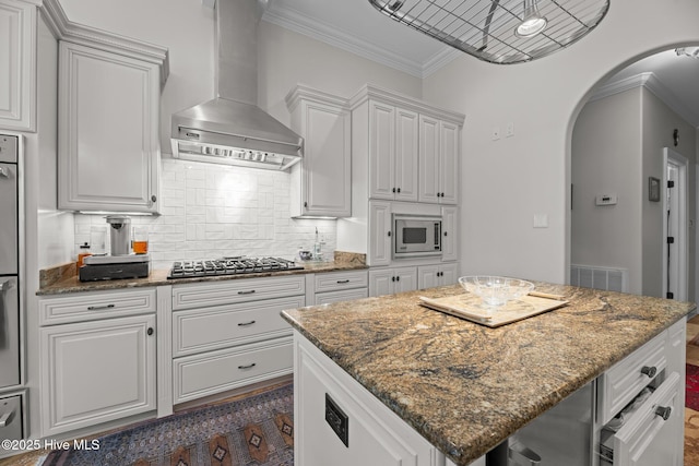 kitchen featuring white cabinets, dark stone counters, a center island, stainless steel appliances, and wall chimney range hood