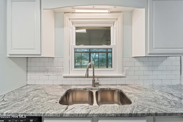 kitchen with tasteful backsplash, white cabinetry, sink, dishwashing machine, and light stone counters