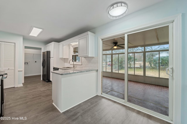 kitchen with sink, white cabinets, light stone counters, a healthy amount of sunlight, and black refrigerator with ice dispenser