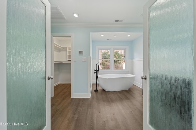 bathroom with ornamental molding, a tub to relax in, and hardwood / wood-style floors