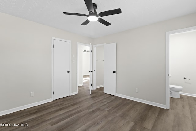 unfurnished bedroom featuring dark wood-style floors, connected bathroom, baseboards, and ceiling fan