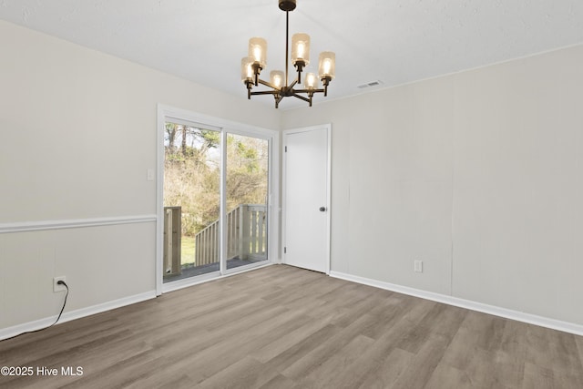 unfurnished dining area featuring a chandelier, wood finished floors, visible vents, and baseboards