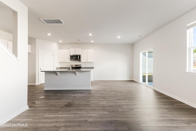 kitchen with dark wood-type flooring, a breakfast bar, white cabinetry, stainless steel appliances, and a kitchen island with sink