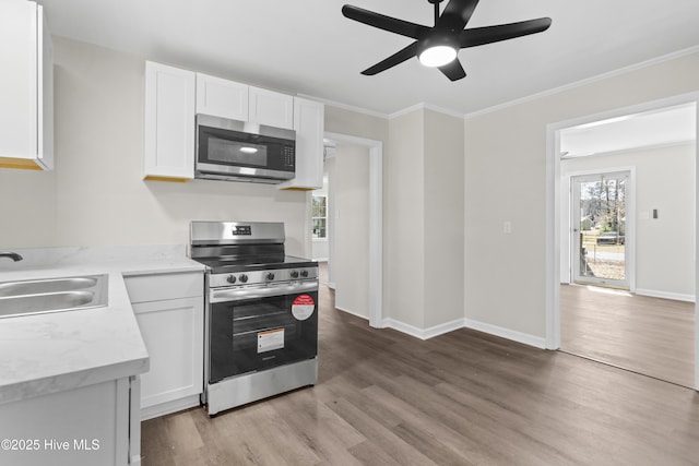 kitchen featuring a sink, white cabinets, appliances with stainless steel finishes, light wood finished floors, and crown molding