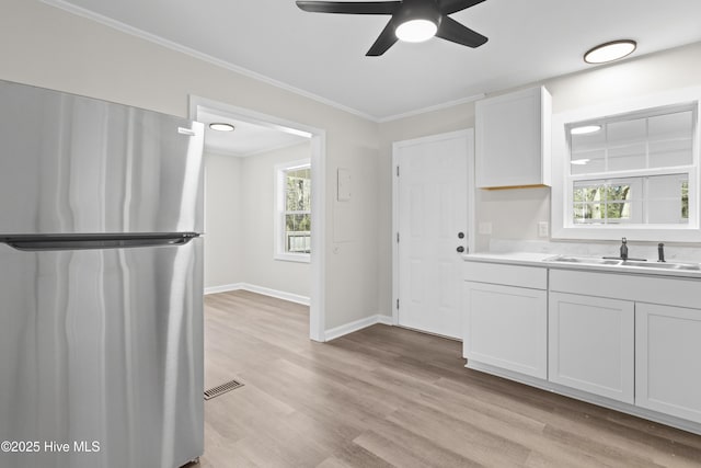 kitchen featuring visible vents, ornamental molding, freestanding refrigerator, light wood-style floors, and a sink