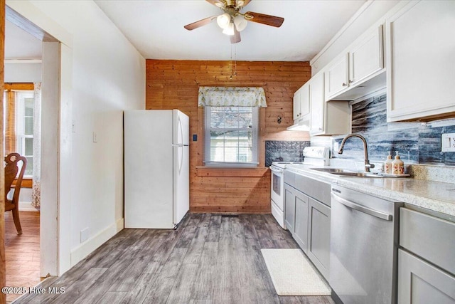 kitchen with wooden walls, white cabinetry, sink, light wood-type flooring, and white appliances