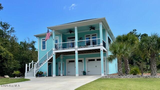 raised beach house with an attached garage, a front lawn, ceiling fan, stairway, and driveway