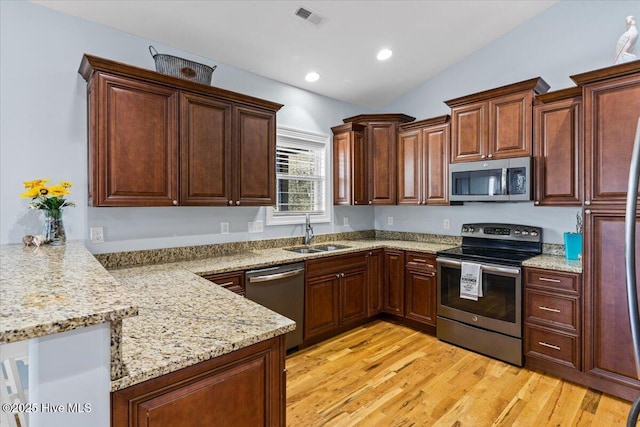 134 NE 11th St, Oak Island, NC 28465 - kitchen with stainless steel appliances, a sink, a peninsula, vaulted ceiling, and light wood-style floors