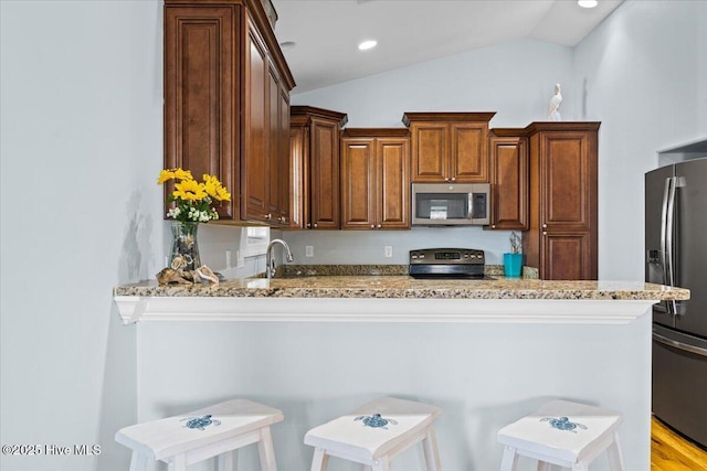 kitchen featuring a kitchen bar, light stone counters, stainless steel appliances, a peninsula, and lofted ceiling