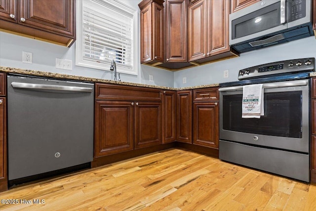 kitchen featuring dark brown cabinetry, light wood-style flooring, stainless steel appliances, and light stone countertops