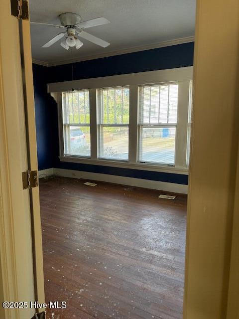 empty room with crown molding, dark wood-type flooring, and ceiling fan