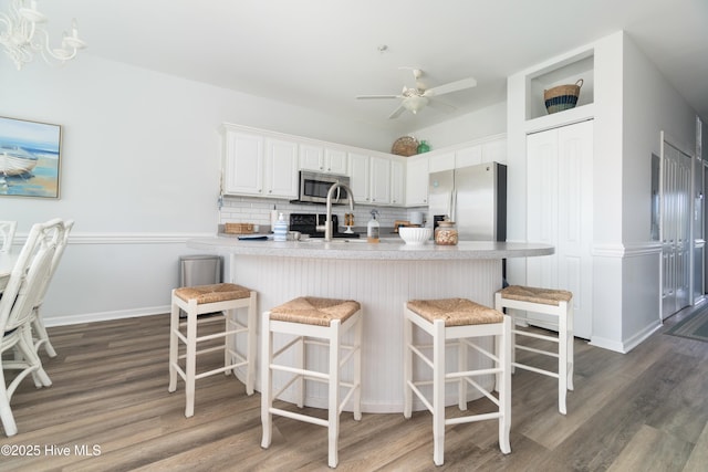 kitchen featuring a breakfast bar area, dark wood-type flooring, appliances with stainless steel finishes, white cabinetry, and decorative backsplash