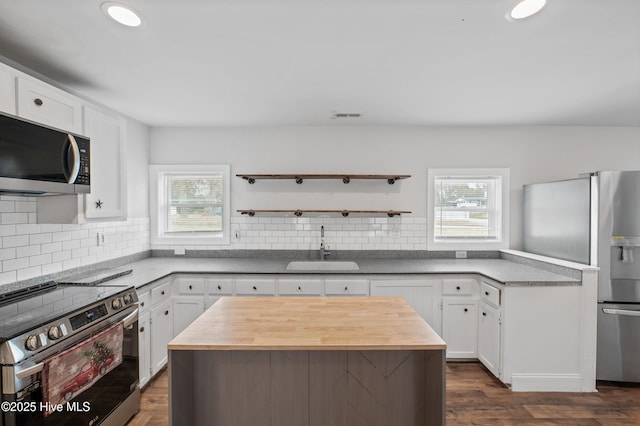 kitchen with sink, appliances with stainless steel finishes, a kitchen island, white cabinets, and backsplash