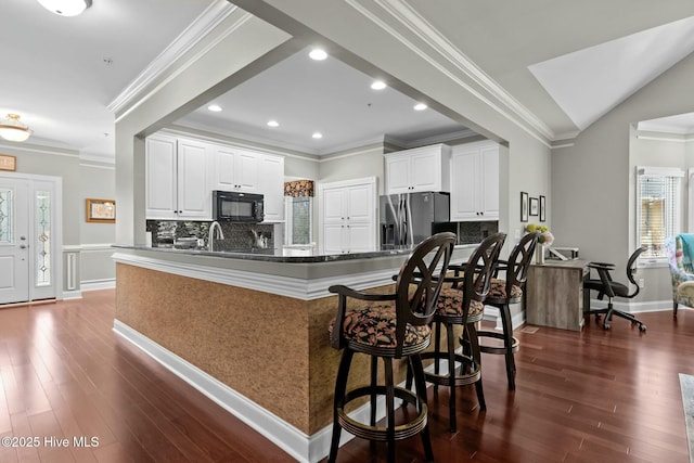 kitchen with stainless steel fridge, white cabinets, a kitchen breakfast bar, a peninsula, and black microwave