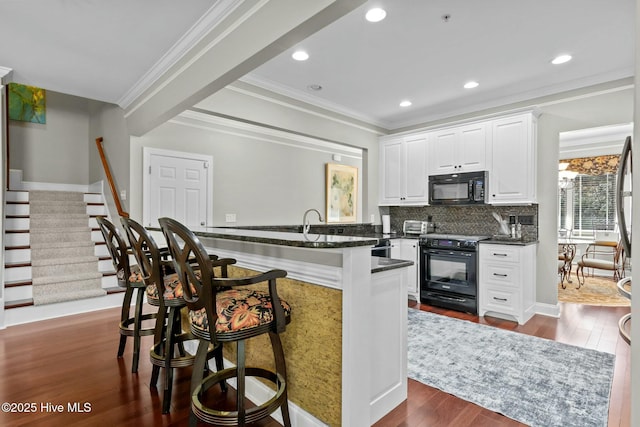 kitchen with dark countertops, white cabinetry, black appliances, a peninsula, and a kitchen bar