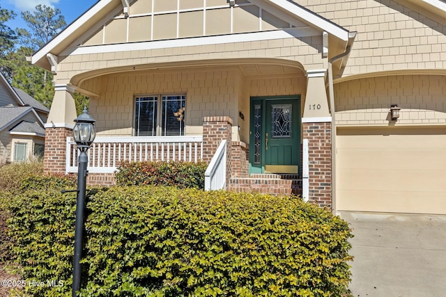 doorway to property featuring a garage, concrete driveway, brick siding, and a porch