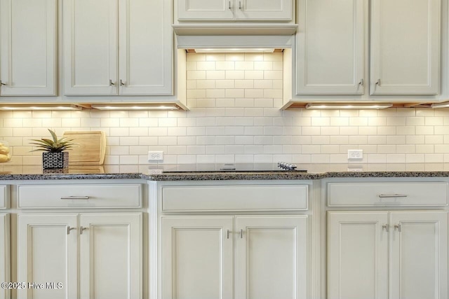 kitchen featuring white cabinetry, decorative backsplash, black electric cooktop, and dark stone counters