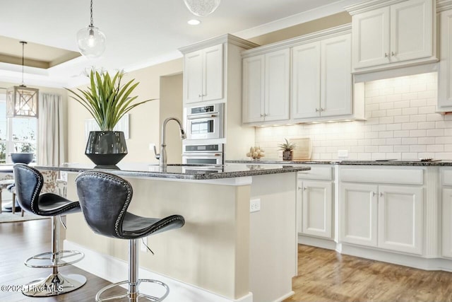 kitchen with white cabinetry, hanging light fixtures, a kitchen island with sink, and light hardwood / wood-style floors