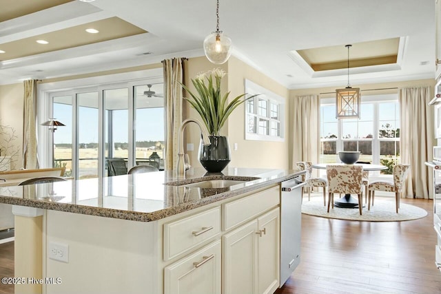 kitchen featuring white cabinetry, an island with sink, hanging light fixtures, a tray ceiling, and light stone countertops