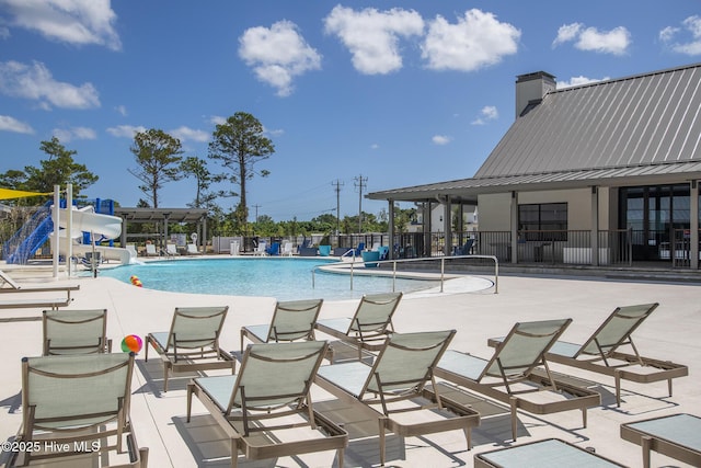 community pool with fence, a water slide, and a patio area
