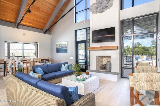 living area featuring a fireplace, high vaulted ceiling, wooden ceiling, wood finished floors, and beamed ceiling