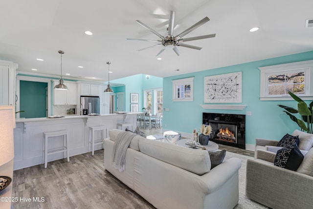 living room with a tiled fireplace, ceiling fan, recessed lighting, and light wood-type flooring
