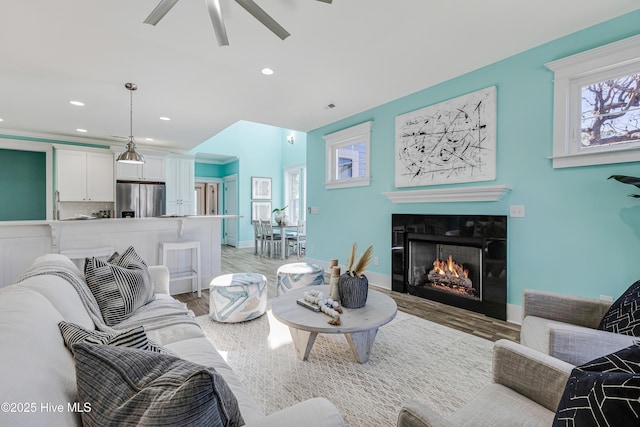 living room featuring light wood-type flooring, baseboards, a lit fireplace, and ceiling fan