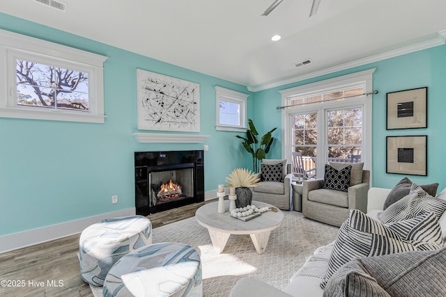 living area featuring ornamental molding, baseboards, visible vents, a warm lit fireplace, and wood finished floors