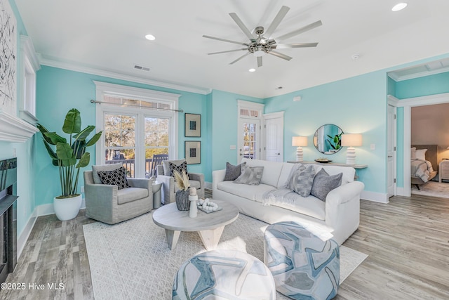 living room featuring crown molding, a ceiling fan, light wood finished floors, a fireplace, and baseboards