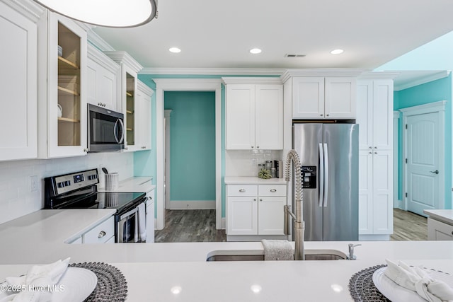 kitchen featuring white cabinets, light countertops, crown molding, wood finished floors, and stainless steel appliances