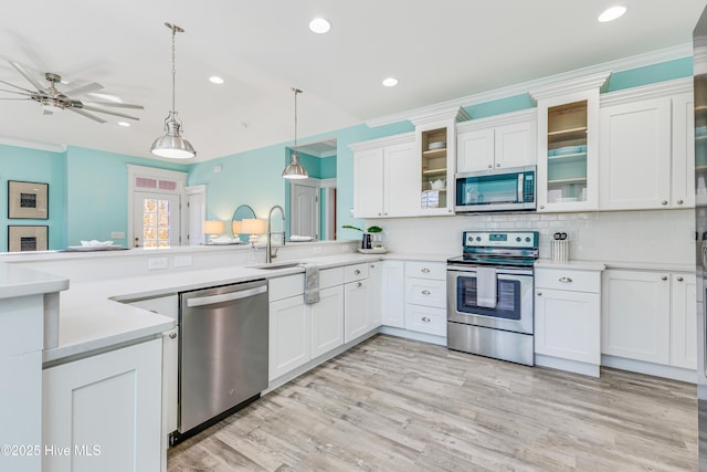 kitchen with a sink, white cabinetry, a peninsula, stainless steel appliances, and decorative light fixtures