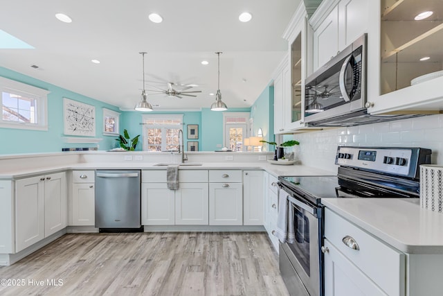 kitchen with light countertops, white cabinets, stainless steel appliances, a sink, and decorative light fixtures