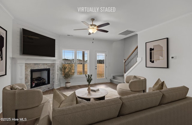 living room with a fireplace, wood finished floors, visible vents, stairs, and crown molding