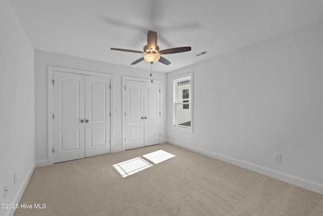 unfurnished bedroom featuring baseboards, visible vents, ceiling fan, carpet flooring, and two closets