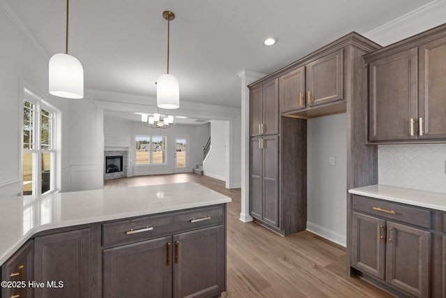 kitchen featuring light wood-type flooring, ornamental molding, backsplash, and decorative light fixtures