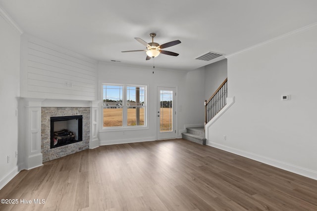 unfurnished living room featuring visible vents, stairway, wood finished floors, and a stone fireplace