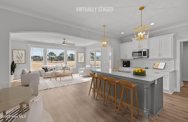 kitchen with a breakfast bar area, a sink, white cabinets, backsplash, and stainless steel microwave