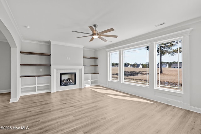 unfurnished living room featuring light wood-style flooring, a fireplace, arched walkways, and crown molding