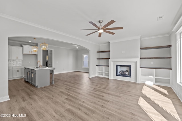 unfurnished living room with light wood finished floors, visible vents, arched walkways, a fireplace, and a sink